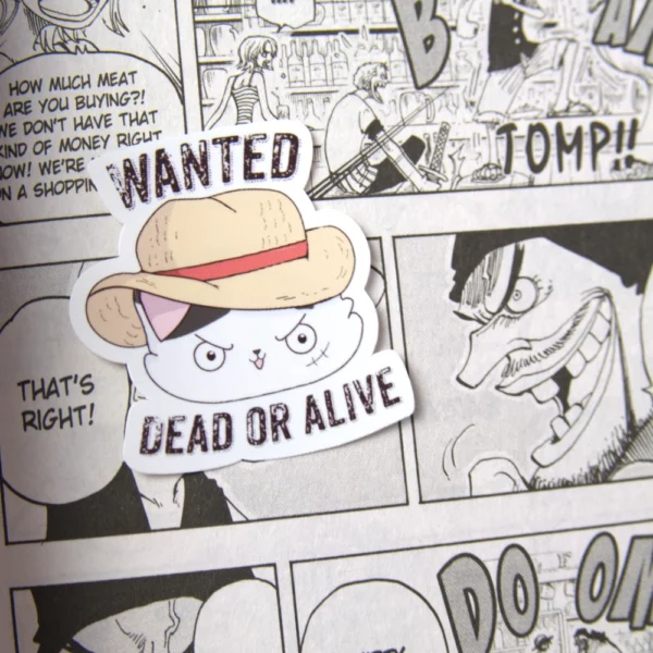 A sticker of a cat in a strawhat with the text wanted dead or alive, lying on top of Luffy in the manga One Piece