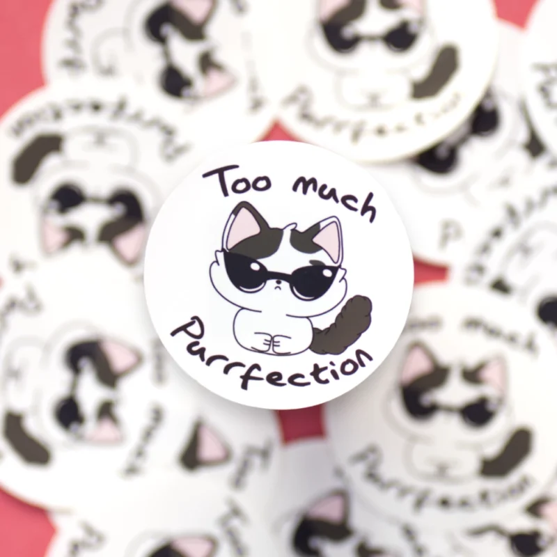 A circular sticker of a cool cat with sunglasses. The text says too much purrfection.