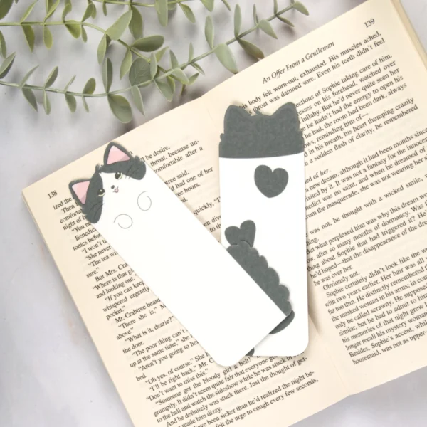Two long bookmarks shaped like cats lying on top of an open book.
