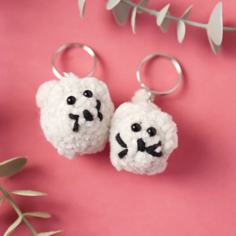 Two crochet cats keychains lying next to each other. The cats are white.