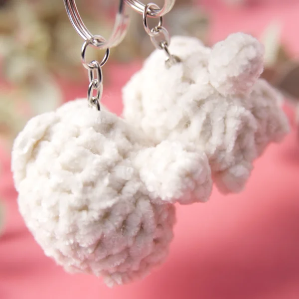 The back and butt of two white crochet cats keychains.