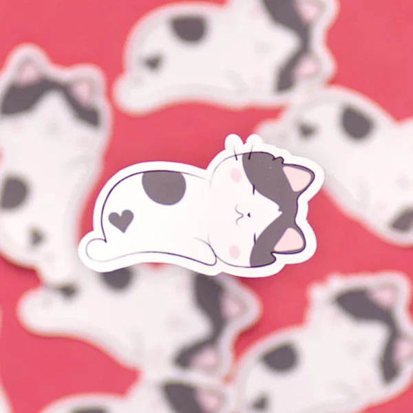 A small sticker of a cute and happy cat sleeping on its belly with a heart shaped spot in its butt.