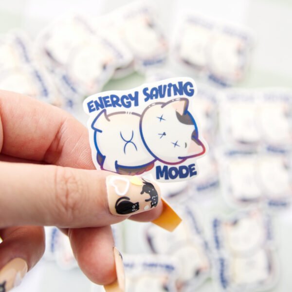 A hand holding a sticker of a cat lying down with a tired expression, accompanied by the text “energy saving mode” above it.