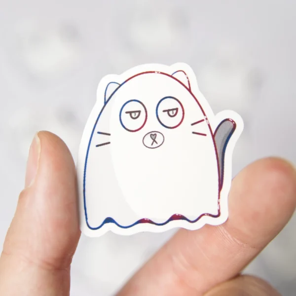 A hand is holding a cat ghost sticker. The cat is looking moderatly annoyed.