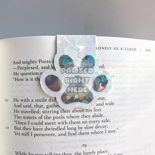 Paw-shaped magnetic bookmark with a colorful, geometric design and the text 'Pawsed Right Here' placed on an open book