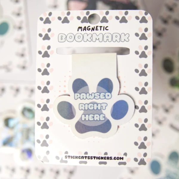 Paw-shaped magnetic bookmark with a colorful, geometric design and the text 'Pawsed Right Here' placed on its backingcard.