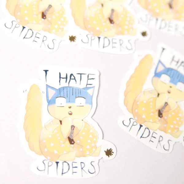A close up of a sticker with a scared yellow cat with the words I hate spiders around the cat.