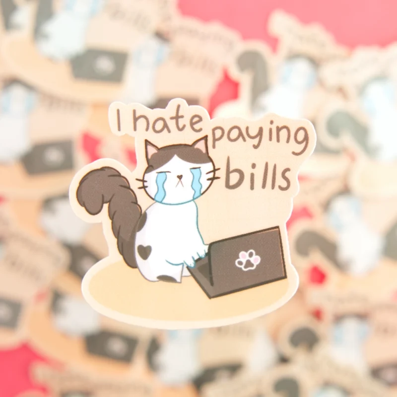 A sticker of a cat crying in front of a computer with the words I hate paying bills over.