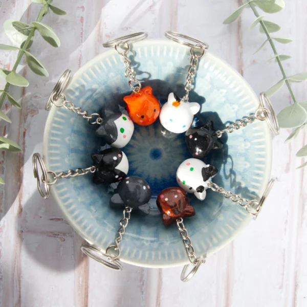 A bowl with polymer clay keychains shaped like cats. There are several colored keychains.