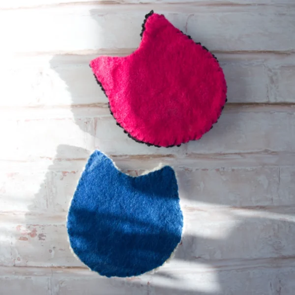 The backing of two cat-shaped mug rugs made with punch needle technique, one is hot pink and the other is saturated blue, featuring playful expressions and pink accents.
