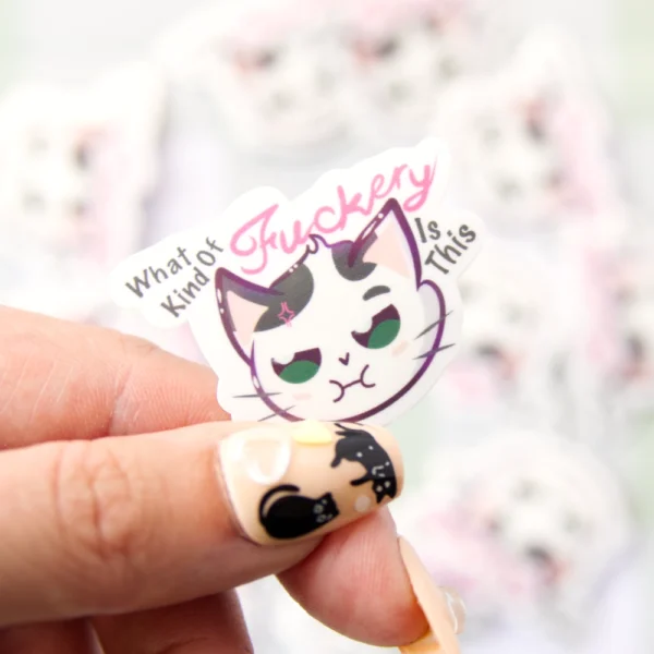 A hand holding a sticker of a cat not looking content with the words what kind of fuckery is this.
