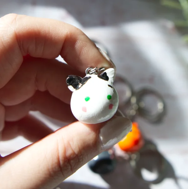 A hand holding in a polymer clay keychan shaped like a cow cat.