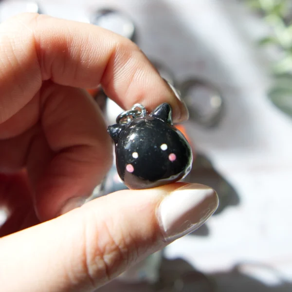 A hand holding in a polymer clay keychan shaped like a black cat.