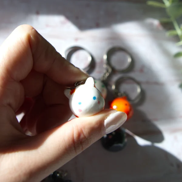 A hand holding in a polymer clay keychan shaped like a calico cat.