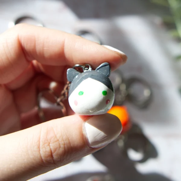 A hand holding in a polymer clay keychan shaped like a grey and white cat.