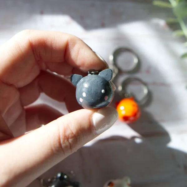 A hand holding in a polymer clay keychan shaped like a grey cat.