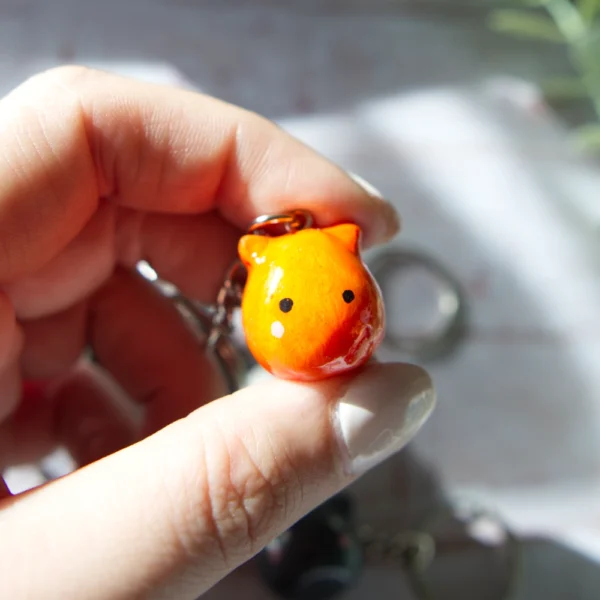 A hand holding in a polymer clay keychan shaped like an orange cat.