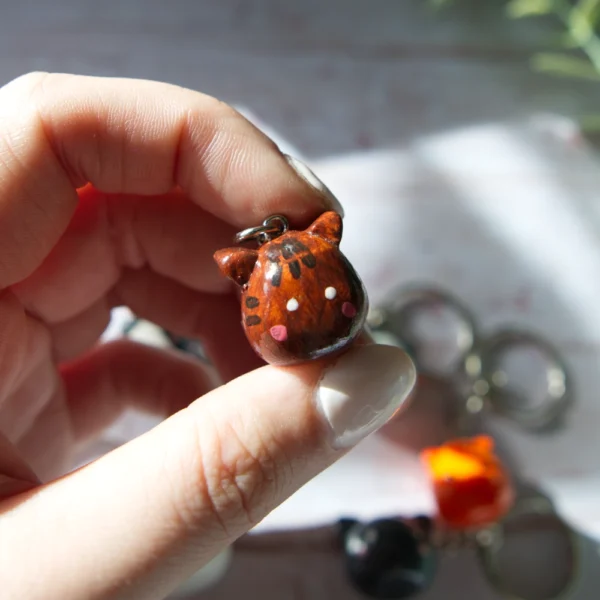 A hand holding in a polymer clay keychan shaped like a tabby cat.