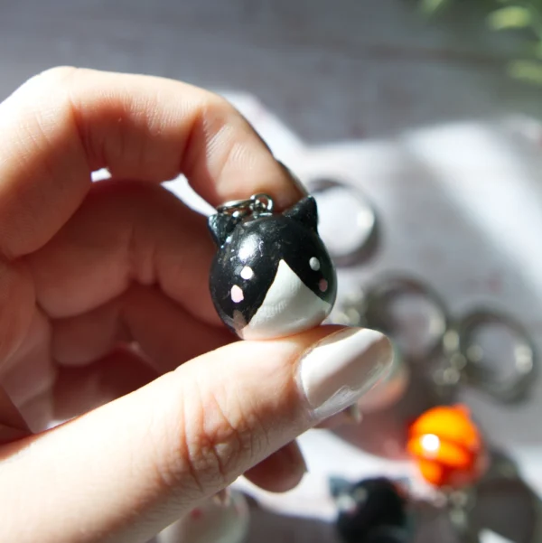 A hand holding in a polymer clay keychan shaped like a tuxedo cat.
