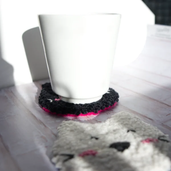 A mug is placed on top of a mug rug, made with punch needle technique, the rugs are black and white.