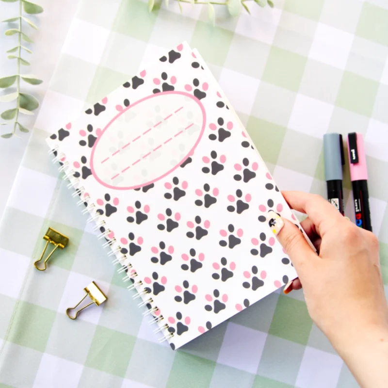 A hand holding a notebook that is decorated with various colored cat paws.