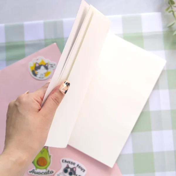 A hand opening a sticker book featuring a cute illustrated cat on the cover, surrounded by stars and playful design elements.