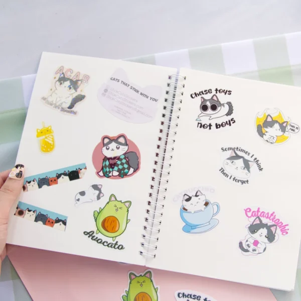A hand opening a sticker book filled with various stickers that looks like cat.